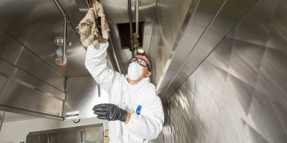 Technician performing kitchen exhaust hood cleaning at a commercial kitchen Technician performing kitchen exhaust hood cleaning at a commercial kitchen