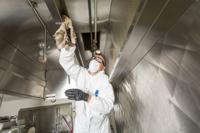 Technician performing kitchen exhaust hood cleaning at a commercial kitchen
